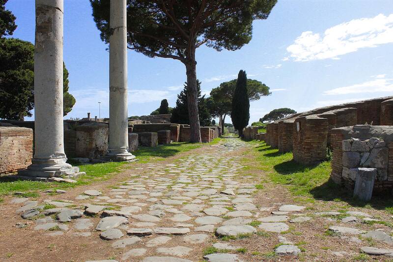 Decumanus Maximus, stone-paved road flanked by ruins, columns and pines